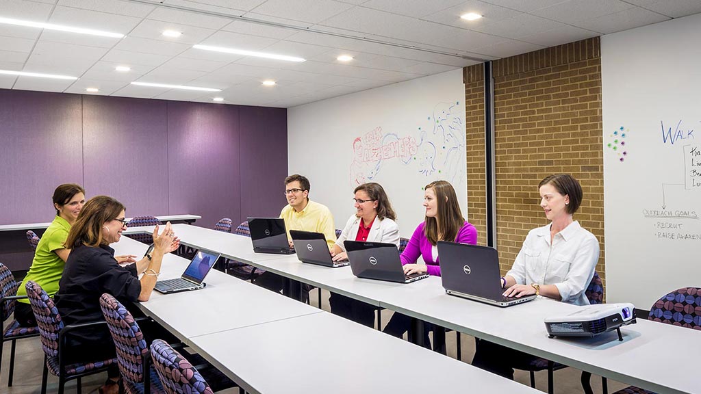 A group of people sitting around a table with laptops.