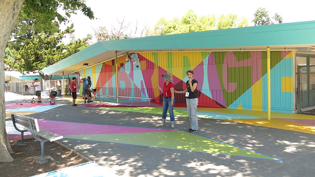 A group of people standing outside a building with a colorful wall.