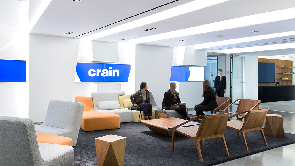 A group of people sitting in a room with chairs and a table.