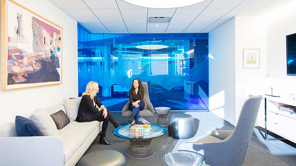 A couple of women sitting in a room with a large window.