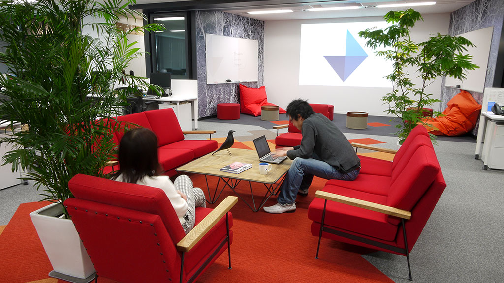 A man and a woman sitting on red couches in a room.