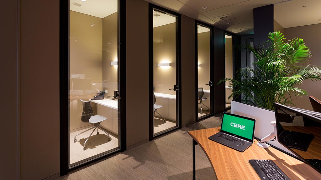A room with a glass door and a desk with a laptop and a plant.