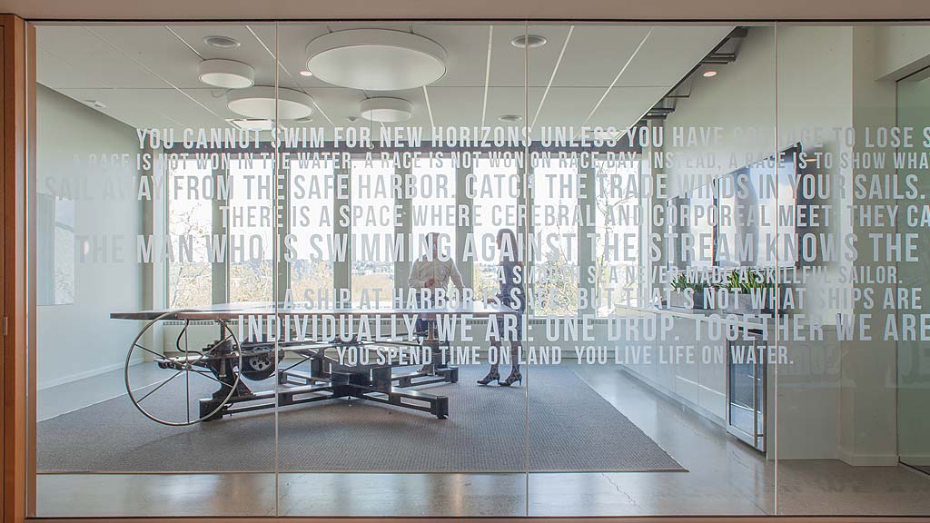 A glass walled room with a few people walking through it.