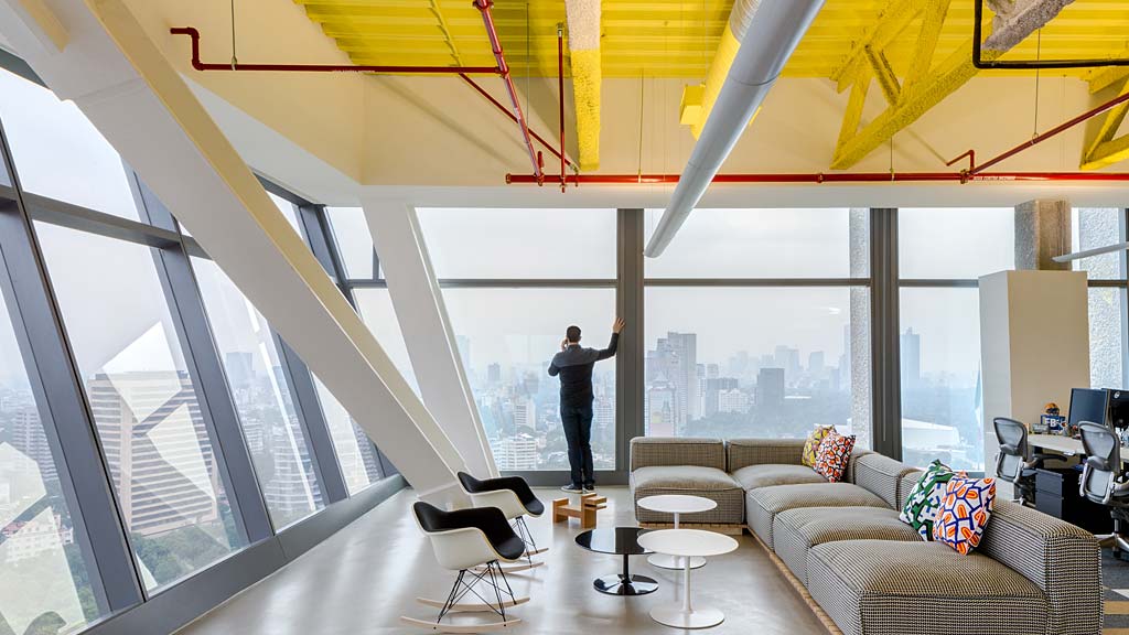 A person standing in a room with a large window and a large view of a city.