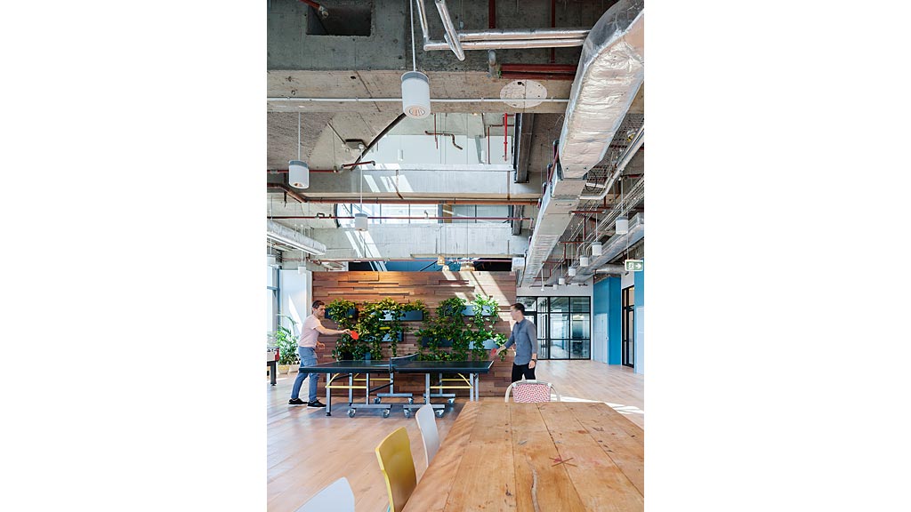 A couple of men standing in a room with a wood floor and a wood floor with a table.