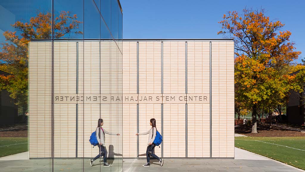 A couple of women walking by a large white building with a fence.