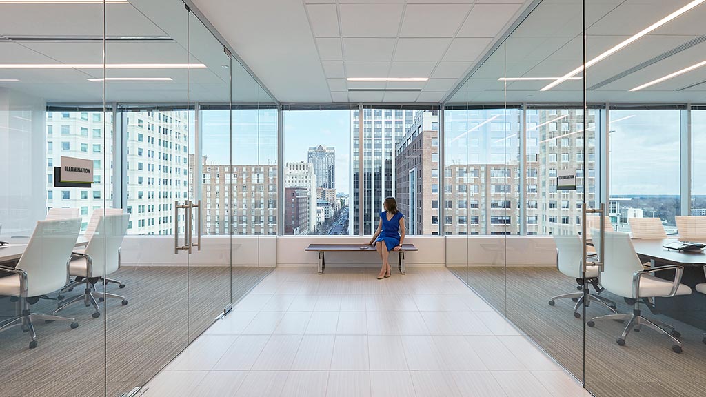 A person sitting on a bench in a large room with large windows.