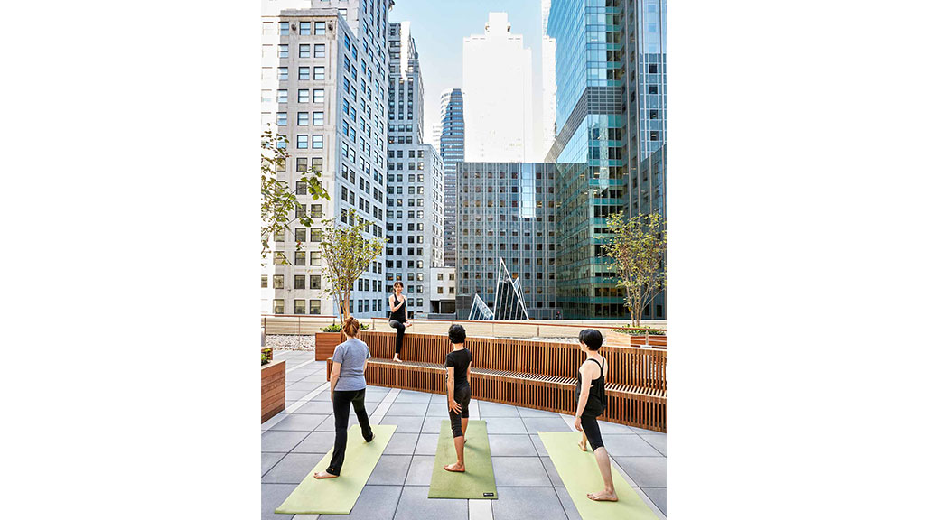 A group of people walking on a sidewalk in front of a fountain.