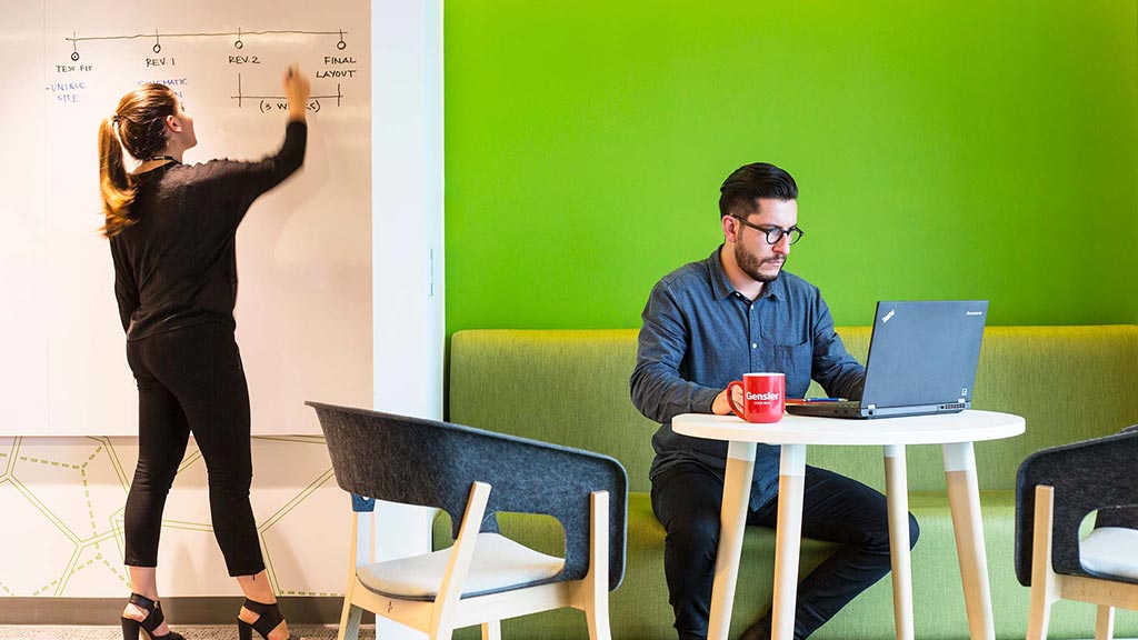 A woman standing next to a man sitting at a desk.