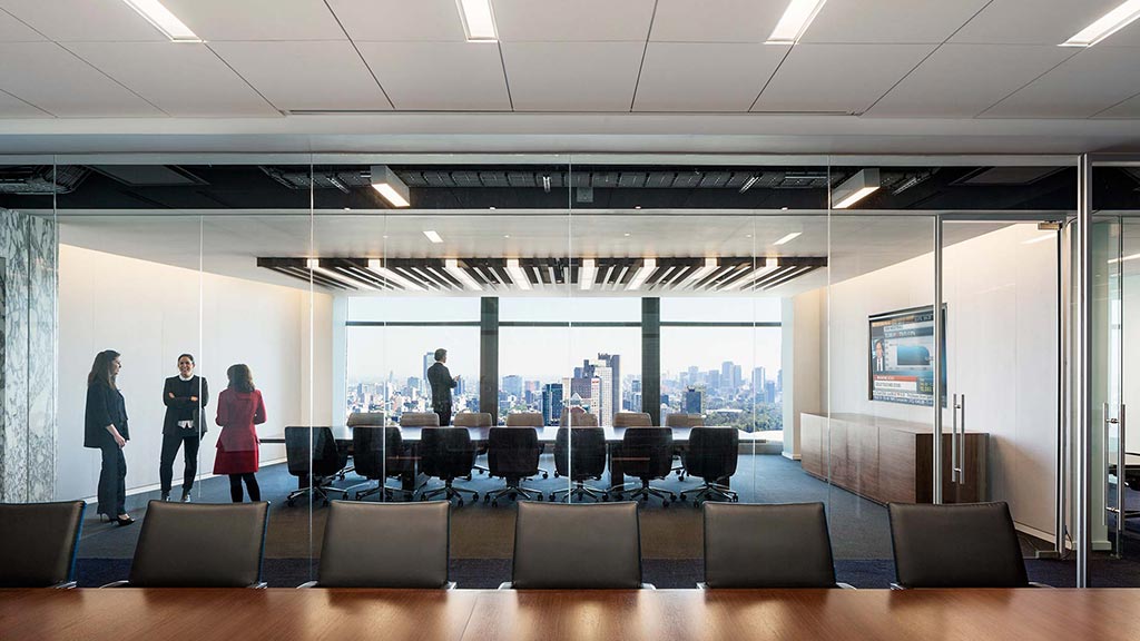 A group of people in a room with a large glass wall and a large window.