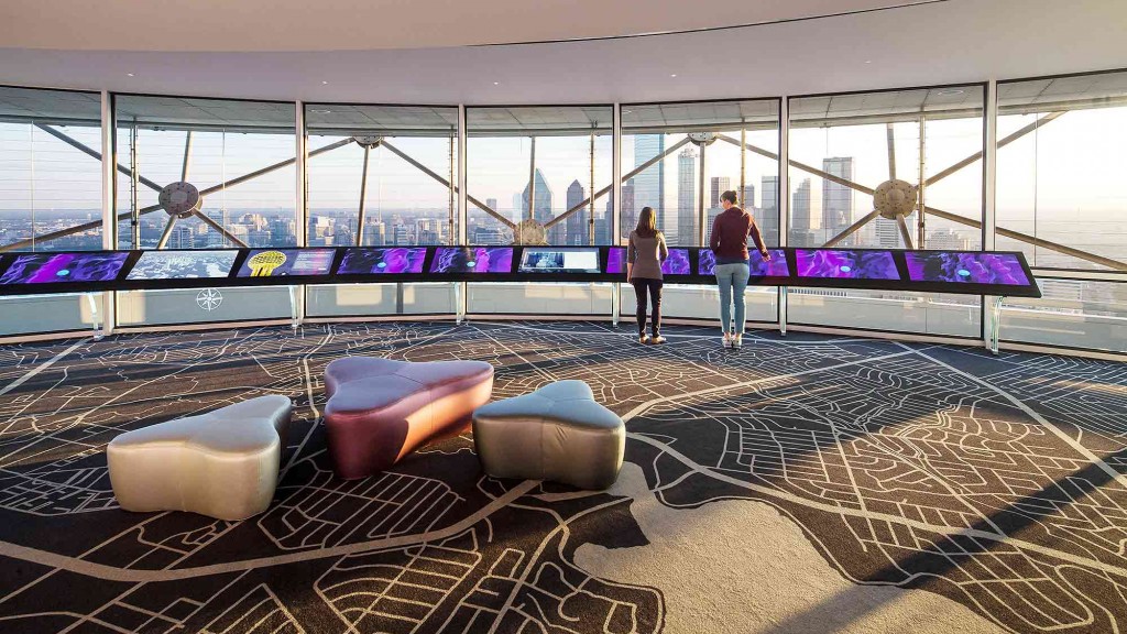 A couple of people standing in a room with large windows.