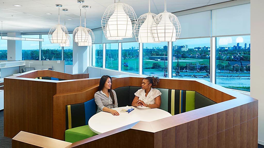 A couple of women sitting at a desk in a large office.