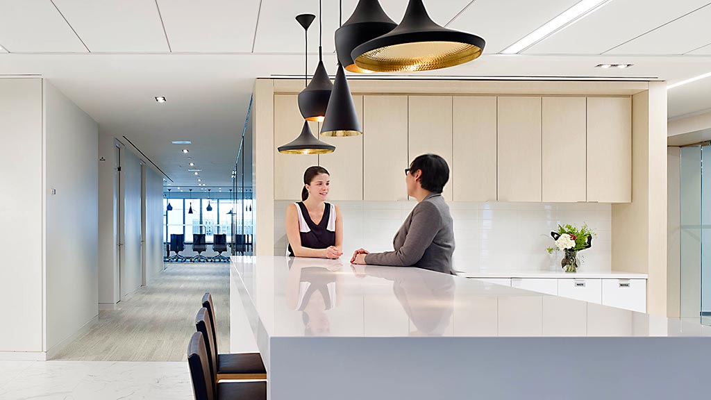 A man and woman sitting at a counter with a couple of lights above them.