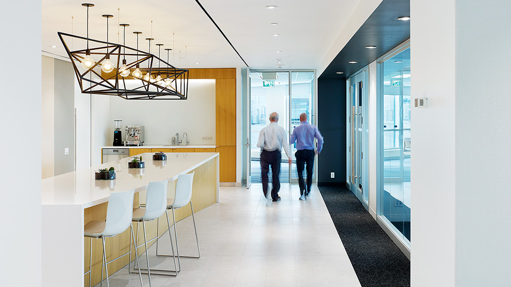 A couple of men walking down a hallway with white chairs and tables.