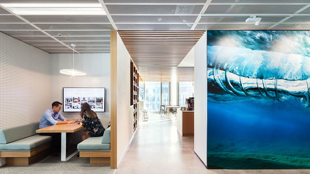 A man and woman sitting at a table in a room with a large blue screen.