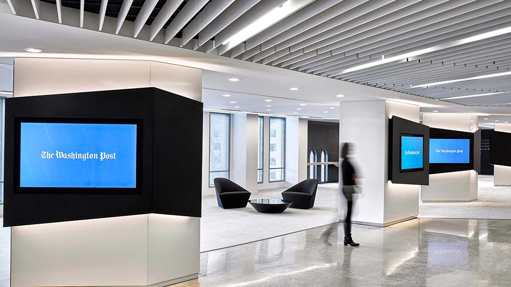 A person standing in a room with a large screen and chairs.