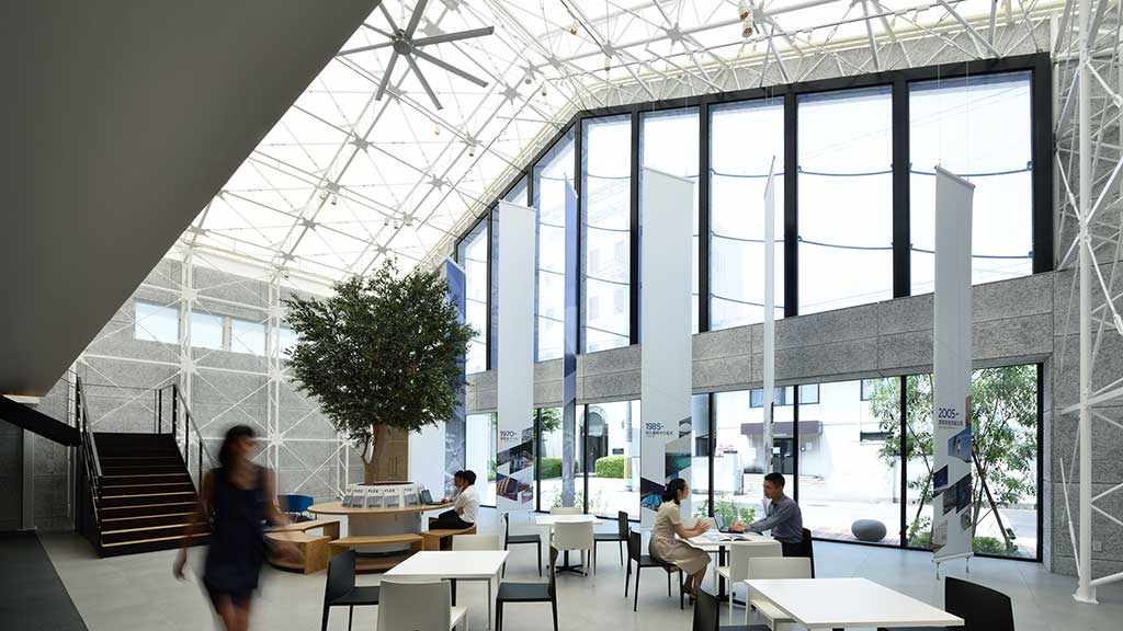 A group of people in a large room with windows and tables.