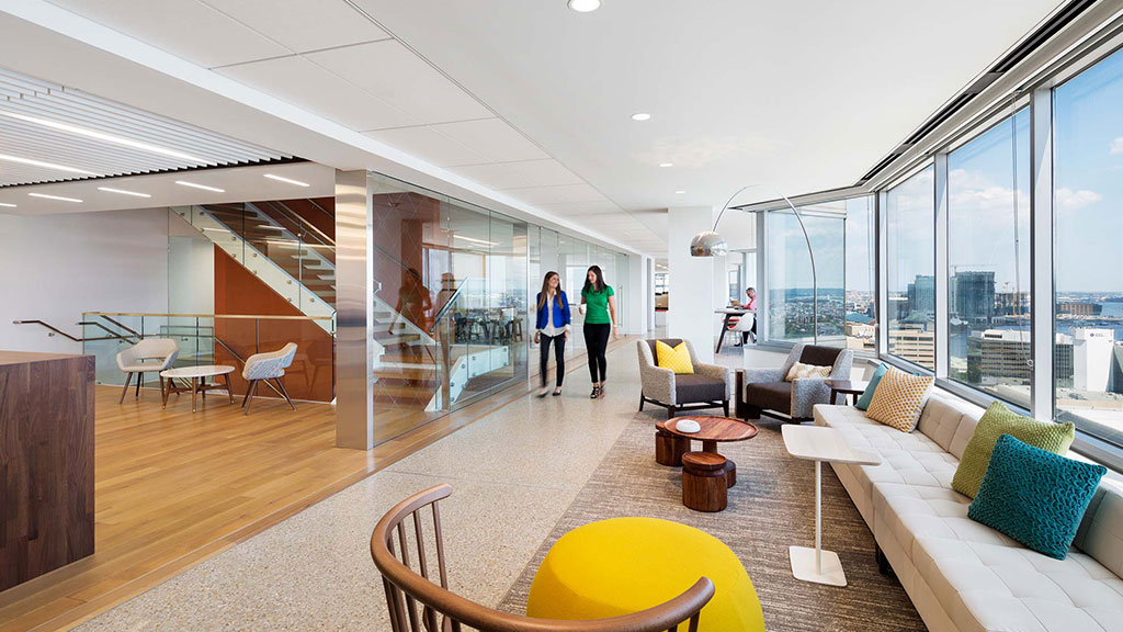 A couple of women walking in a large room with large windows.