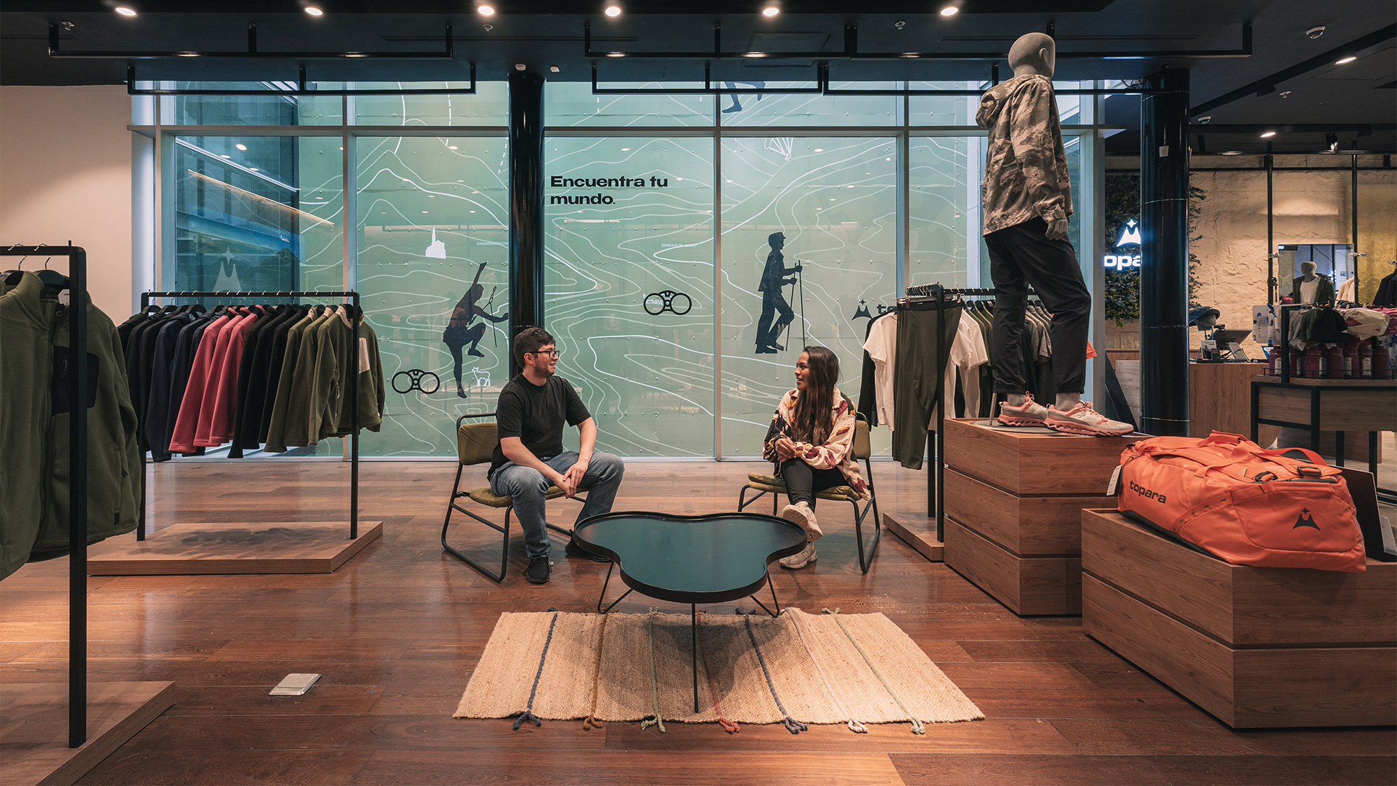 A man and woman sitting in a room with a display of clothing.
