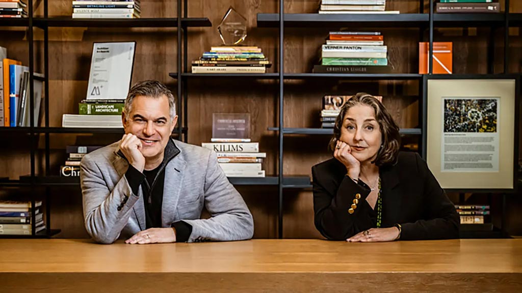 A man and a woman sitting at a table in front of a book shelf.