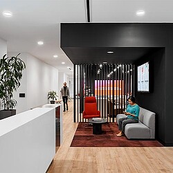 A woman sitting on a couch in a room with a tv and a man standing in the background.