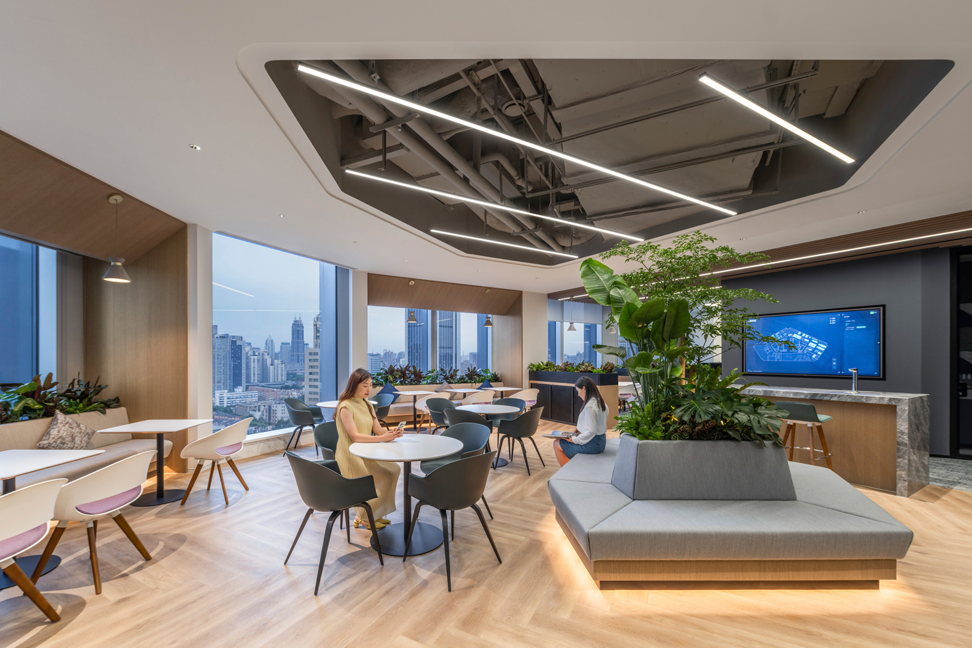 A couple of women sitting at a table in a room with a large window and a large plant.