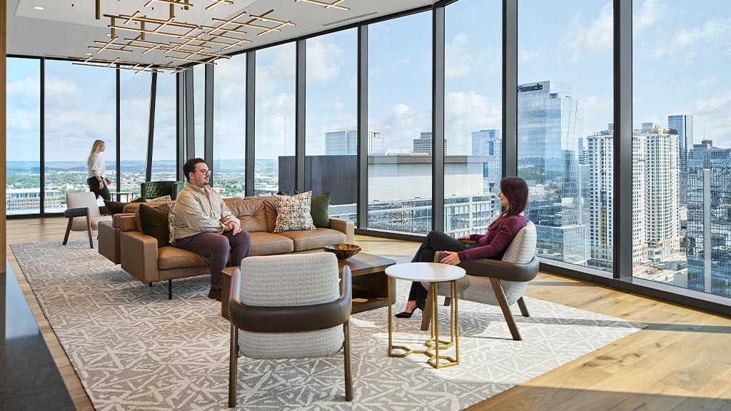 A man and woman sitting on a couch in a room with large windows.
