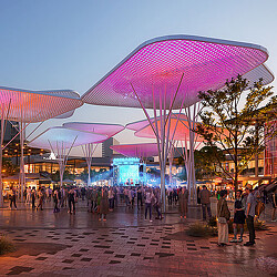 A group of people walking under a building with many umbrellas.
