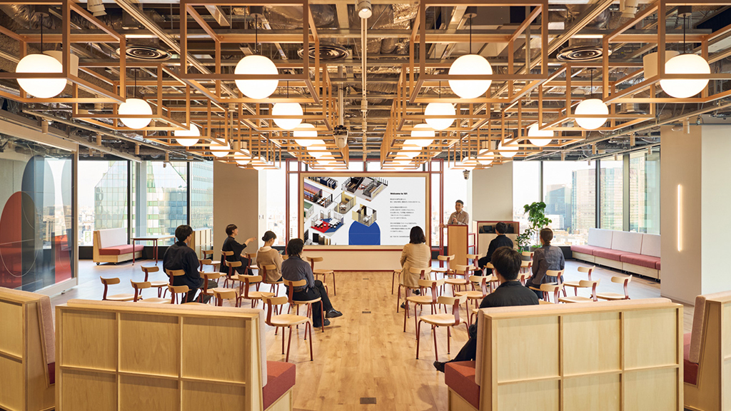 A group of people sitting at tables in a room with large windows.