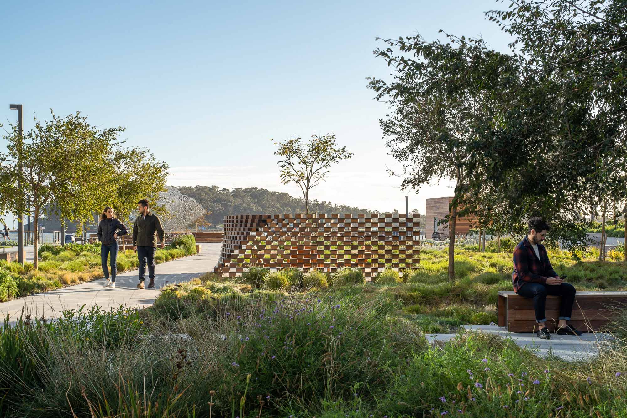 A group of people walking on a path with a brick wall and trees.
