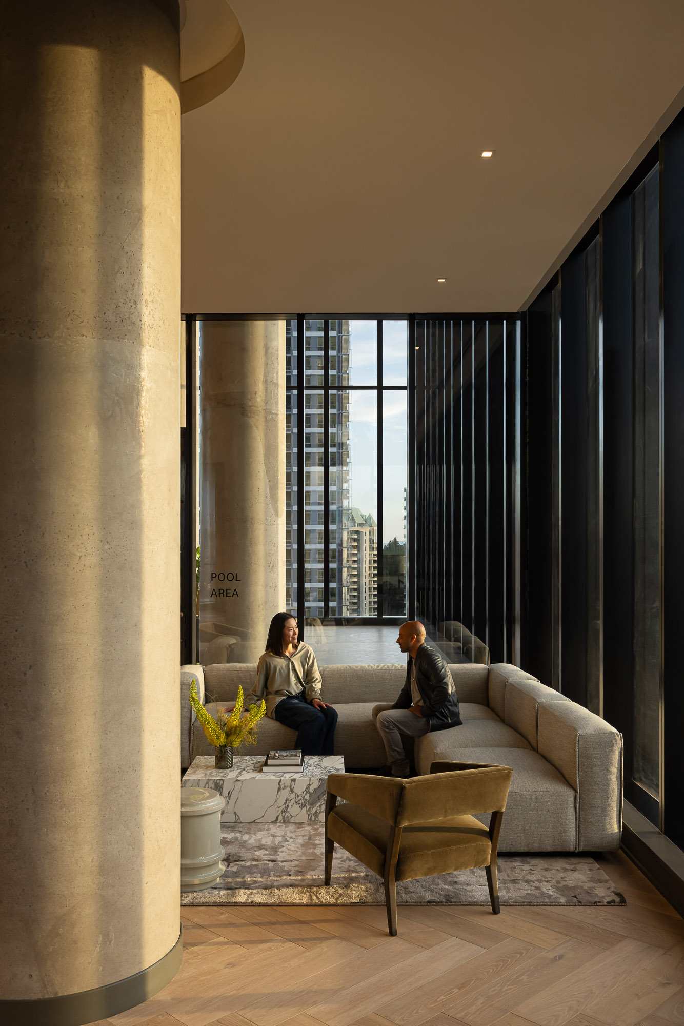 A man and woman sitting on a couch in a room with large windows.