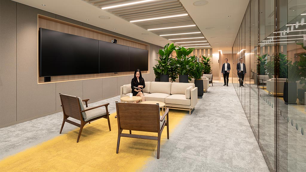 A person sitting on a couch in a room with people walking by.