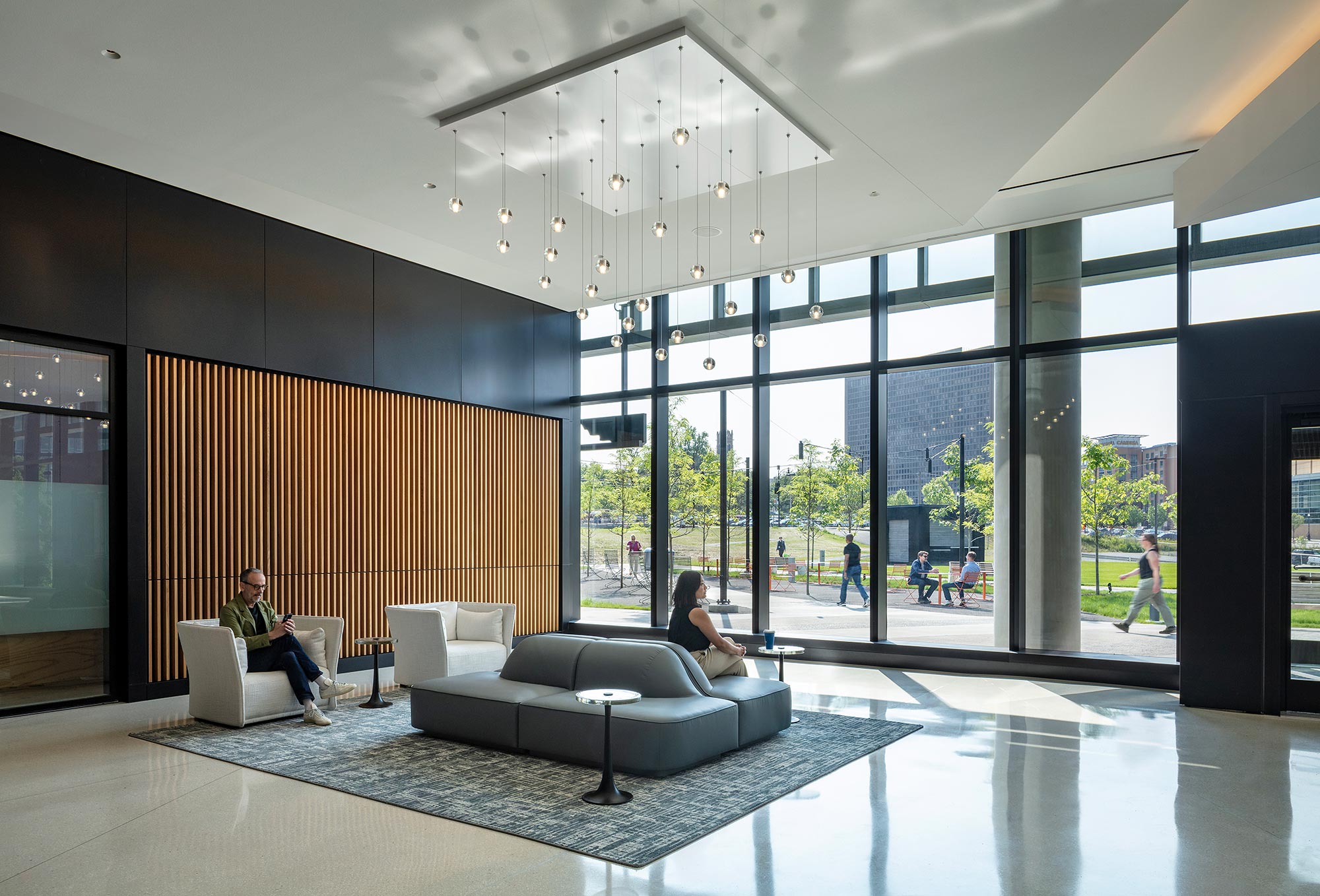 A man and woman sitting on a couch in a large room with large windows.