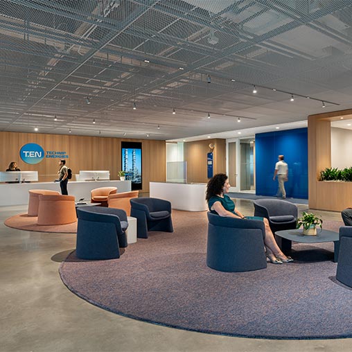 A woman sitting on a chair in a large room with a man standing in the background.