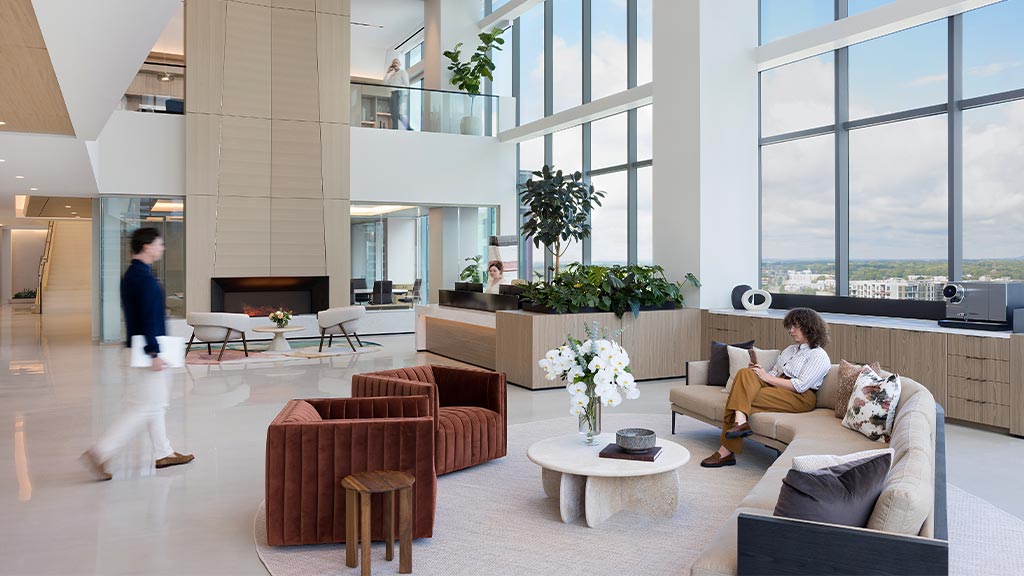 A person sitting on a couch in a large room with large windows.