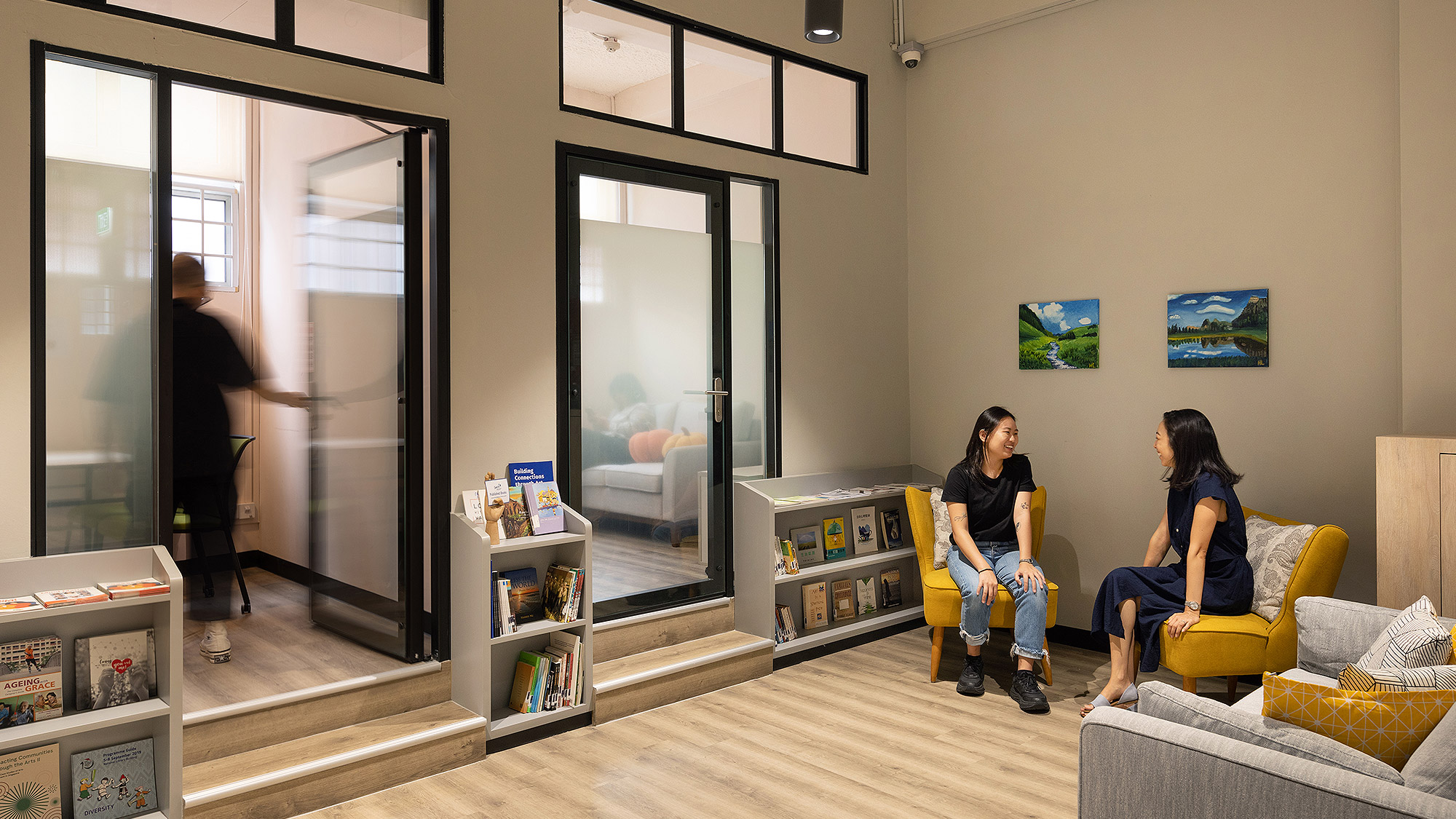 A couple of women sitting on a couch in a room with glass doors.
