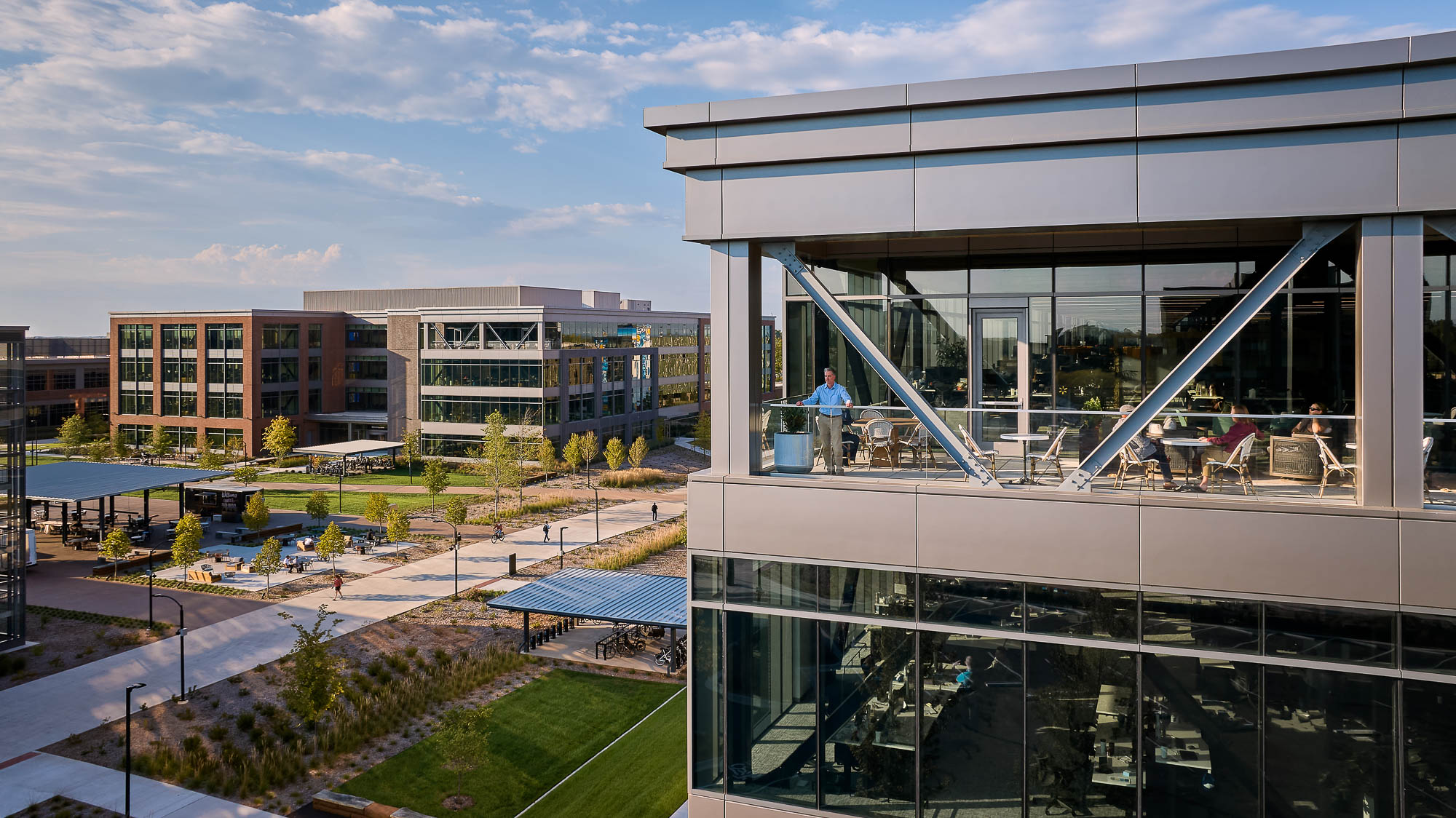 A building with glass walls and a courtyard with people sitting on a bench.