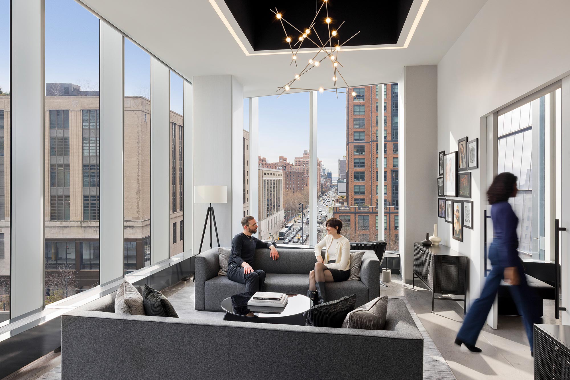 A woman standing in a room with a man sitting on a couch.