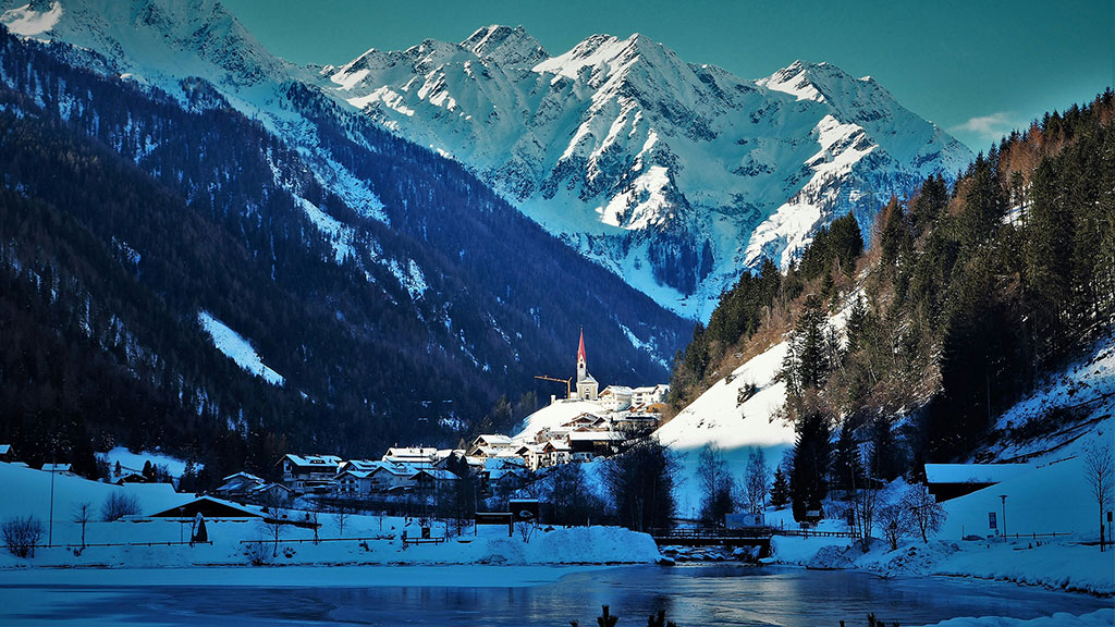 A snowy mountain side with a building and trees and a lake.