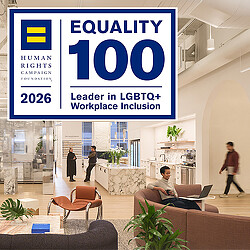 A person sitting in a chair in a room with people walking around.