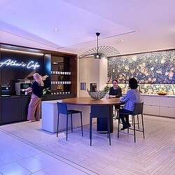 A group of people sitting at a table in a room with a large painting on the wall.