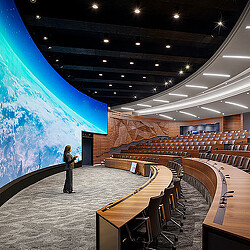 A person standing in a large room with a large blue screen.