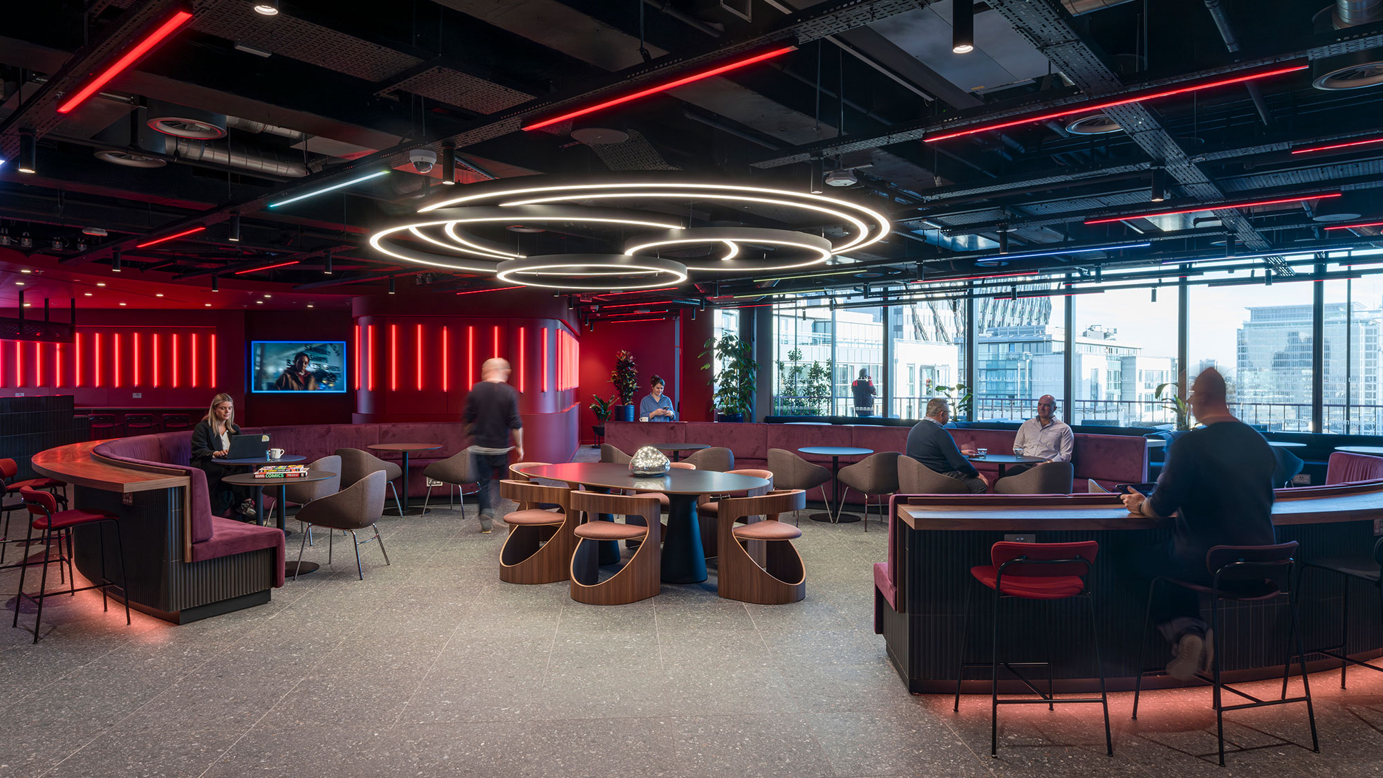 A group of people sitting at tables in a room with large windows.