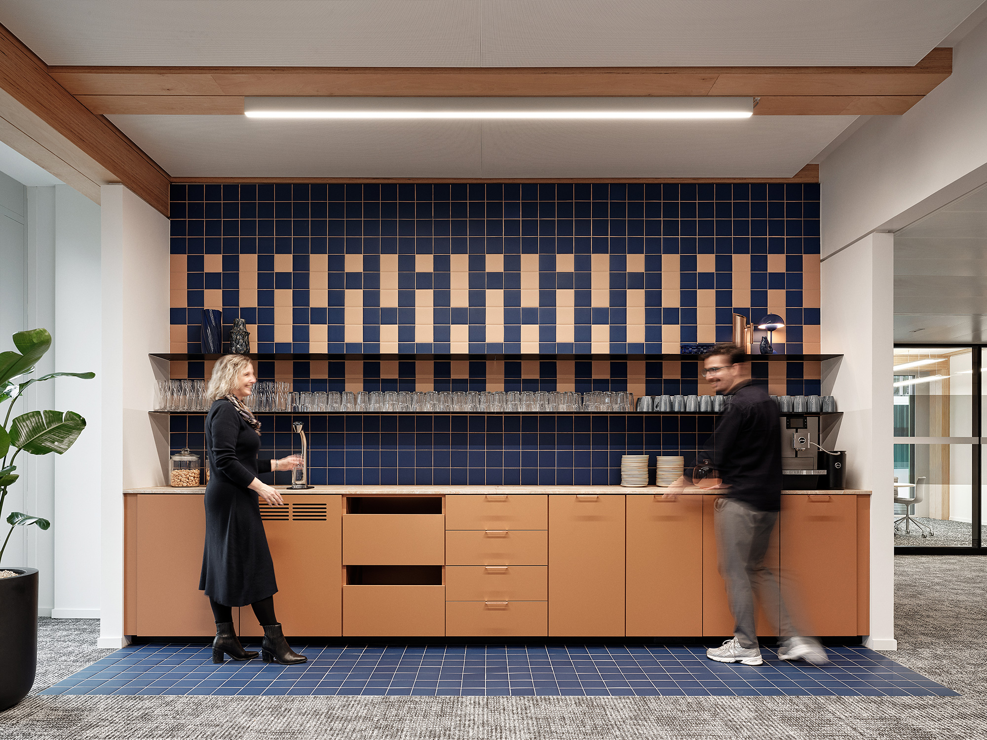 A man and woman standing in front of a counter with a checkered wall behind them.