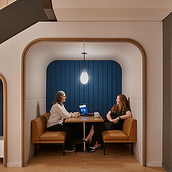 A couple of women sitting at a table looking at a laptop.