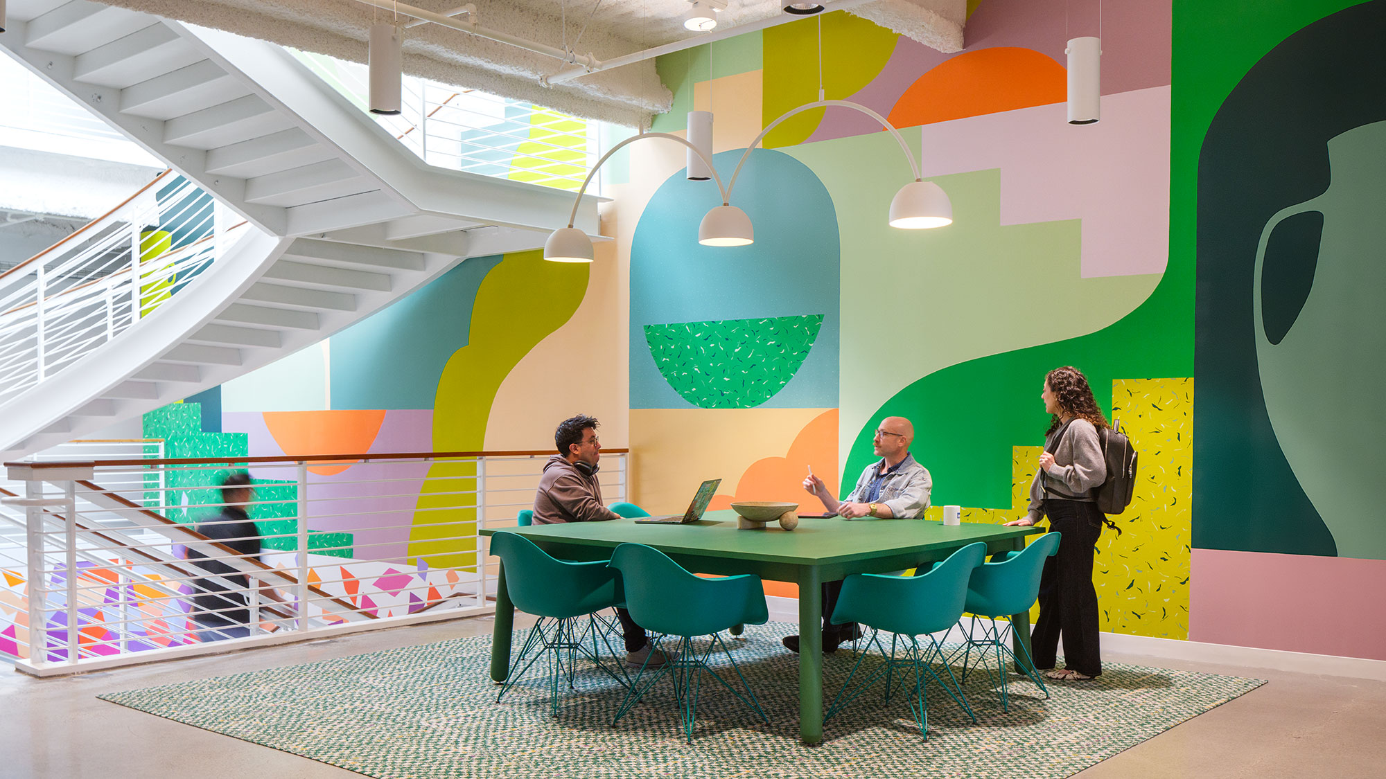 A group of people sitting at a table in a room with a large colorful wall.