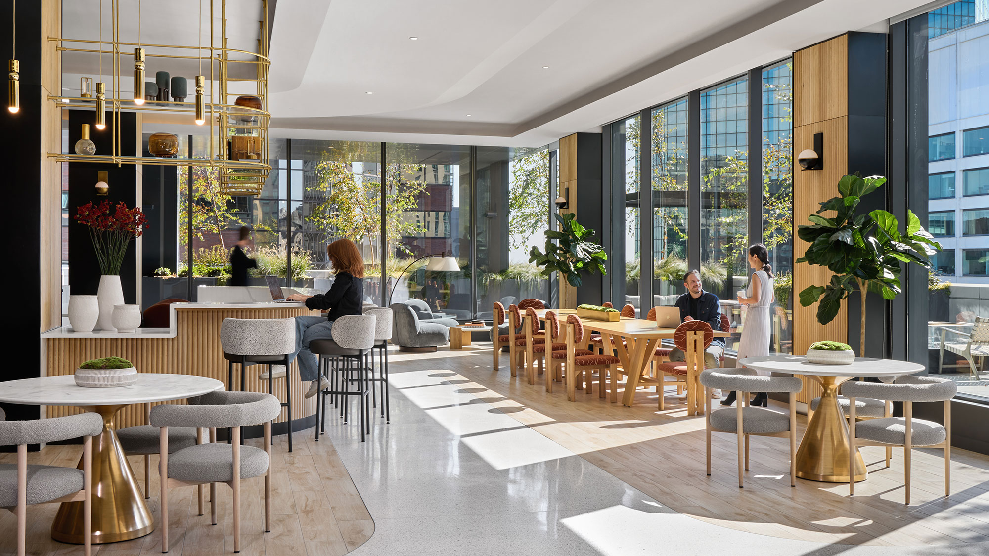 A group of people sitting at tables in a large room with windows.