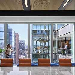 A person standing in a room with a large window and a large glass wall with a city skyline.
