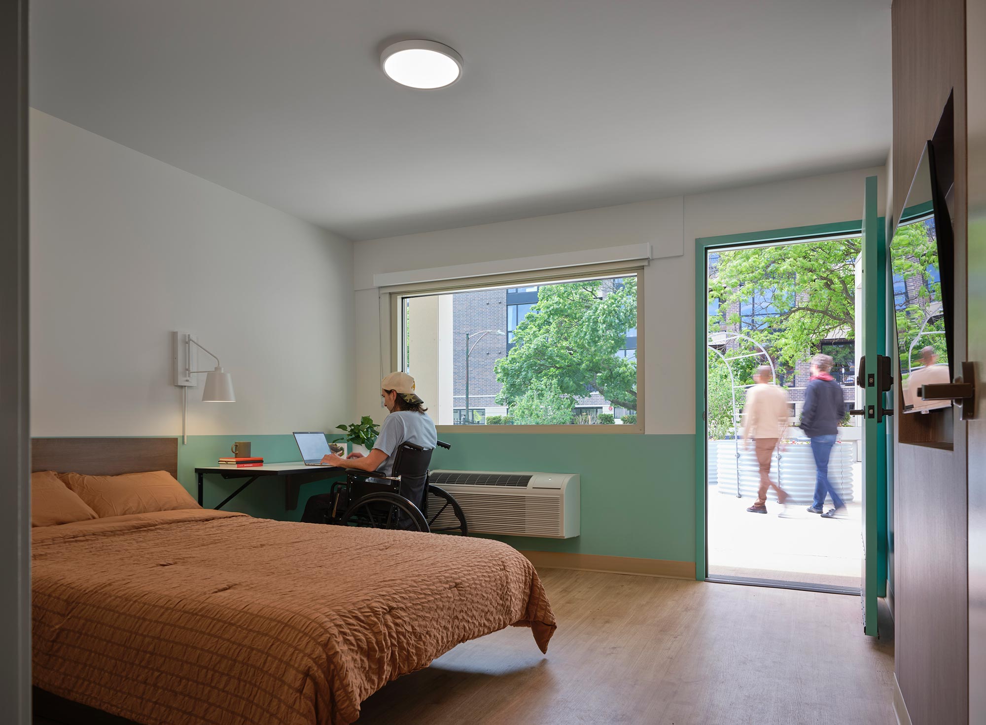 A person sitting on a chair in a room with a bed and a table.
