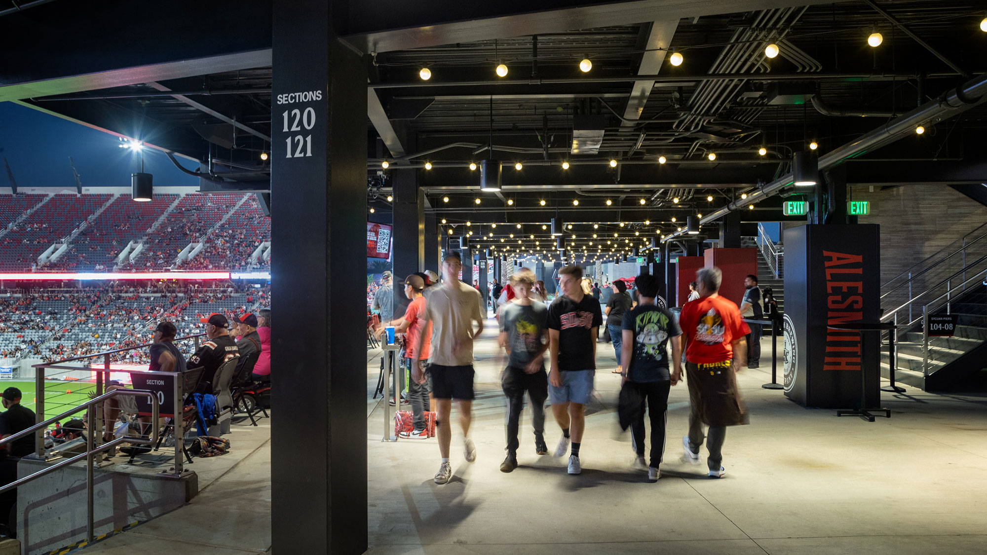 A group of people walking in a large room with people sitting and standing.